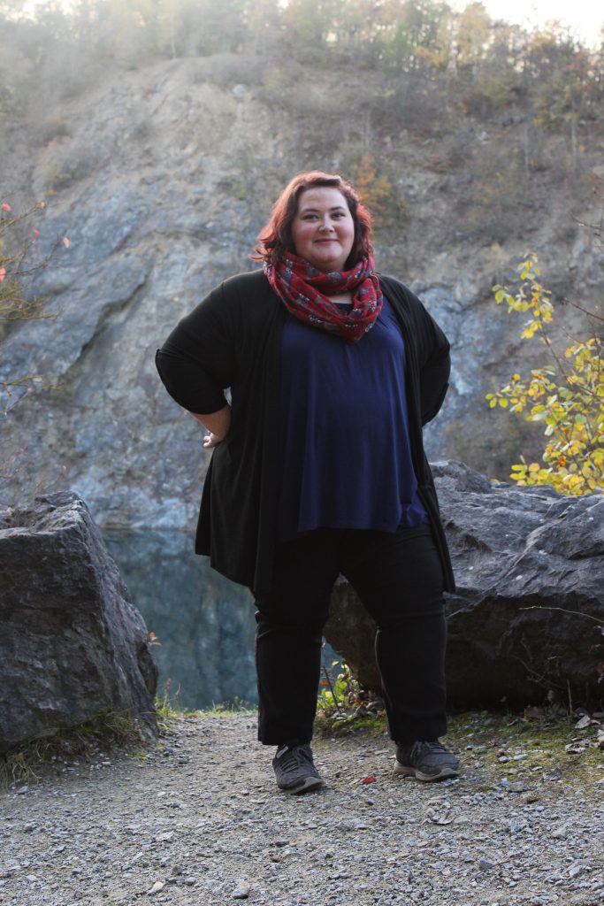 Nadine steht selbstbewusst vor einem Steinbruch und hat die Hände in die Hüften gelegt. Zuversichtlich schaut sie in die Kamera.